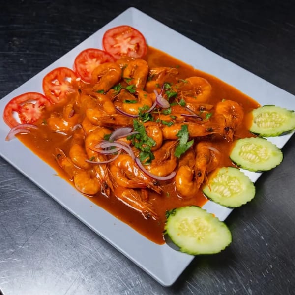 Shrimp in a rich red sauce, garnished with sliced tomatoes, red onions, and cucumbers.