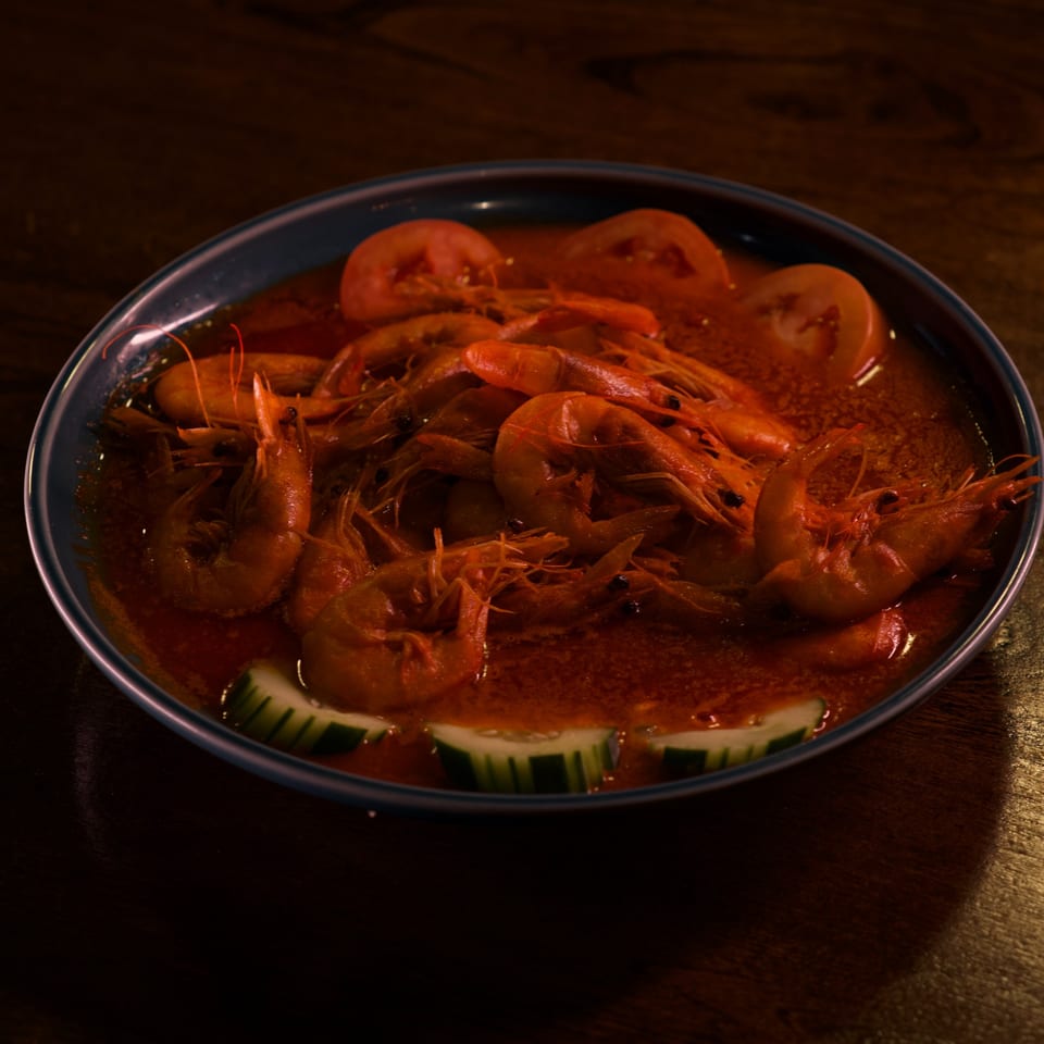 A blue bowl filled with Mariscos La Riviera Nayarit's shrimp in red sauce, garnished with tomato and cucumber.