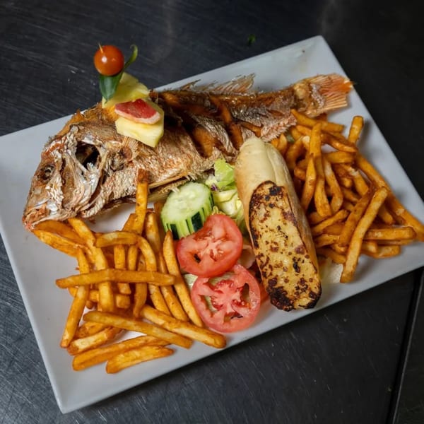 Whole fried fish with french fries, garlic bread, and a side salad on a white rectangular plate.