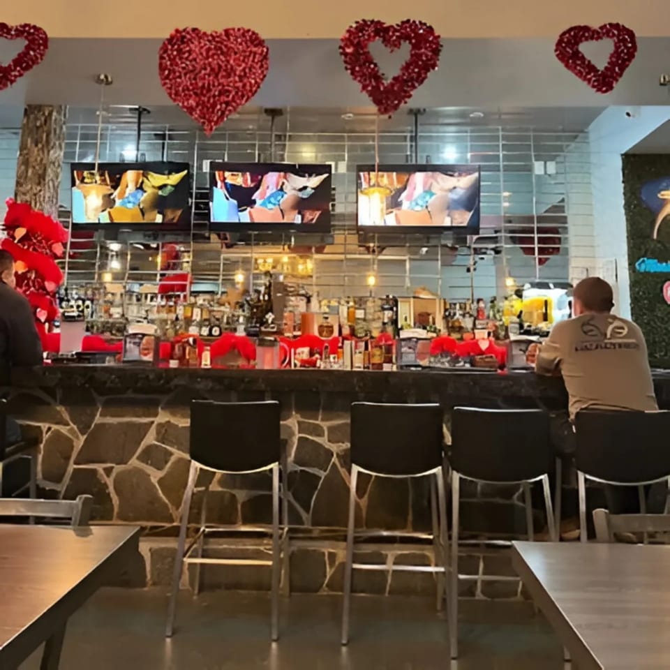 A bar at Mariscos La Riviera Nayarit with red heart decorations, TVs, and patrons.