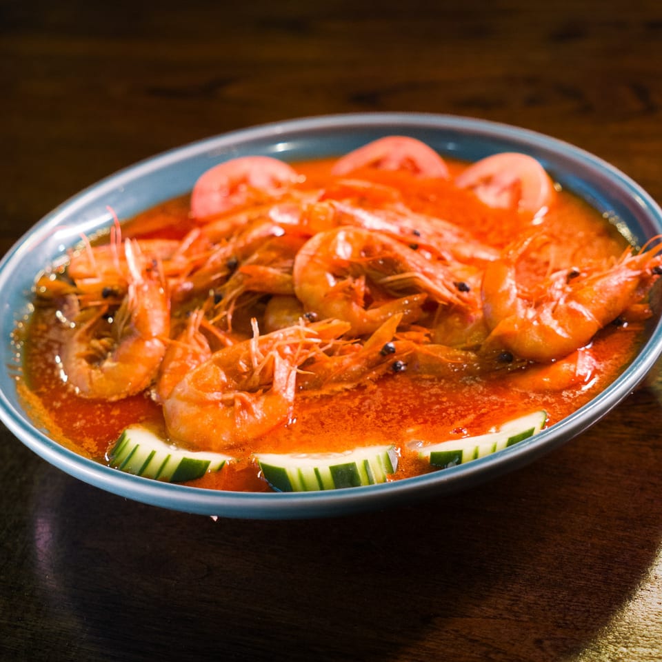 A blue bowl filled with Mariscos La Riviera Nayarit's shrimp dish, garnished with tomato and cucumber slices.