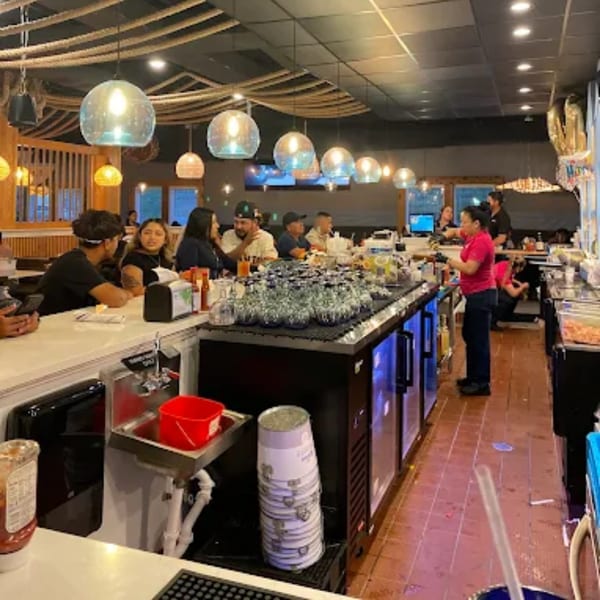 Diners seated at a long bar in a lively seafood restaurant with nautical decor and staff working.