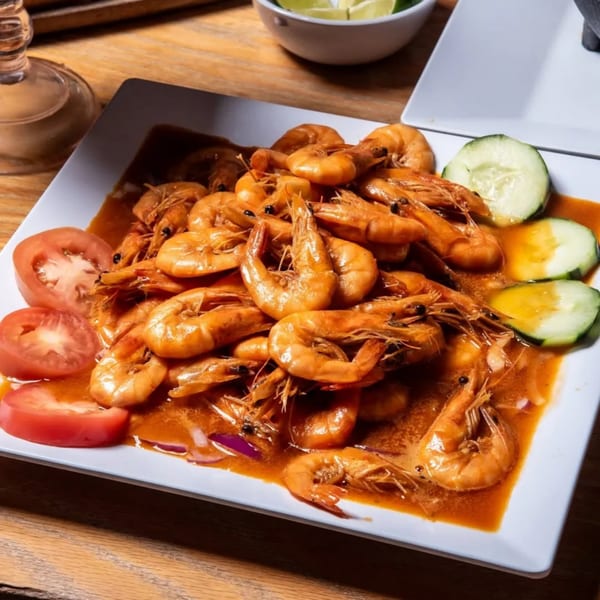 A white rectangular plate filled with shrimp in a red sauce, garnished with tomato and cucumber slices.