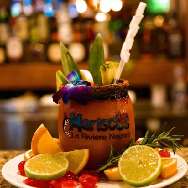 A michelada in a clay mug with the Mariscos La Riviera Nayarit logo, garnished with fruit and a flower.