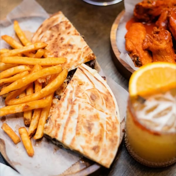 Quesadillas with french fries, buffalo wings, and an orange juice drink with an orange slice.