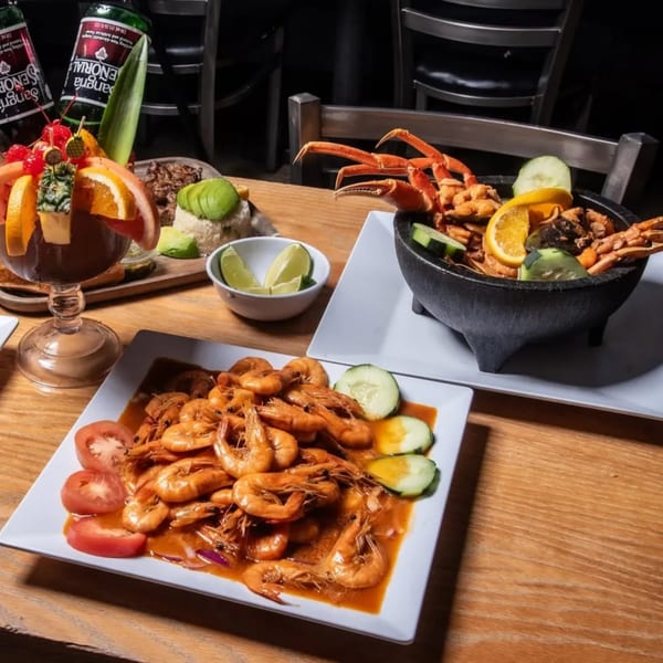 A table laden with various seafood dishes, including shrimp, crab, and a molcajete, with drinks.