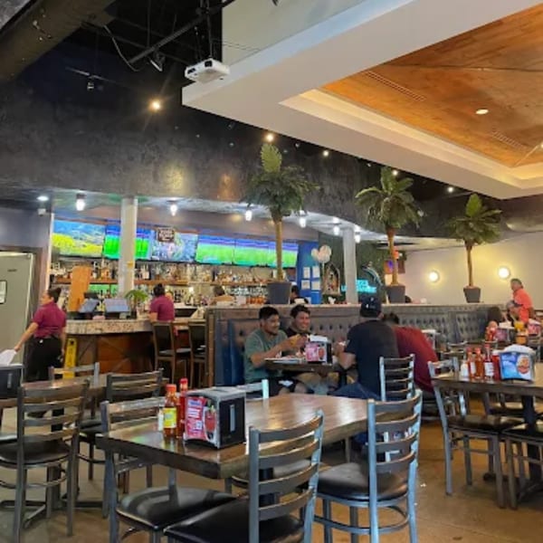Interior of Mariscos La Riviera Nayarit, showing dining tables, a bar with TVs, and patrons.